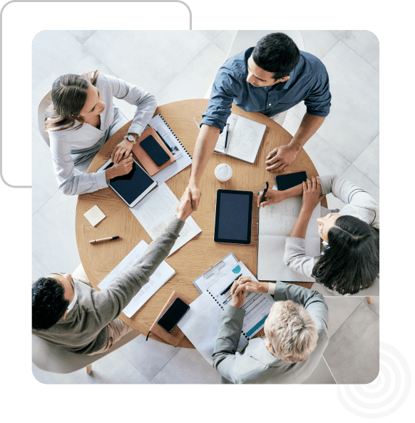 Group 93 Five people sit around a round table with notebooks, tablets, and phones, engaged in a meeting. Two individuals shake hands.